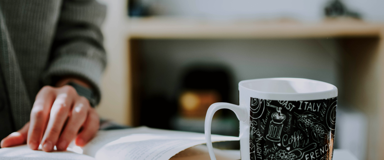 man reading a book in front of the glass of coffee